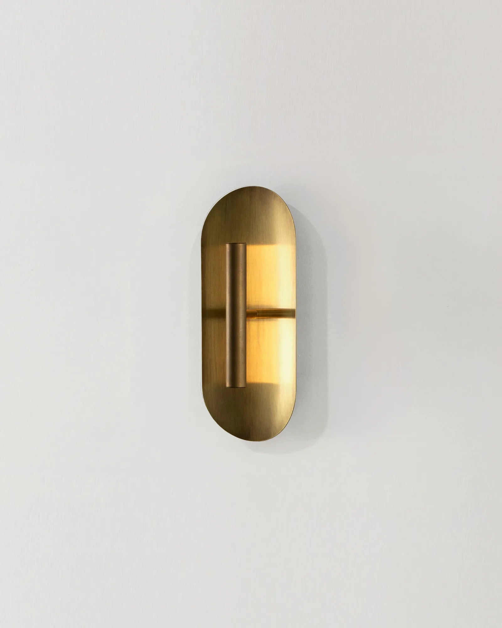 A minimal wall light with a curved, metallic reflector design in a brass finish, mounted on a white wall.