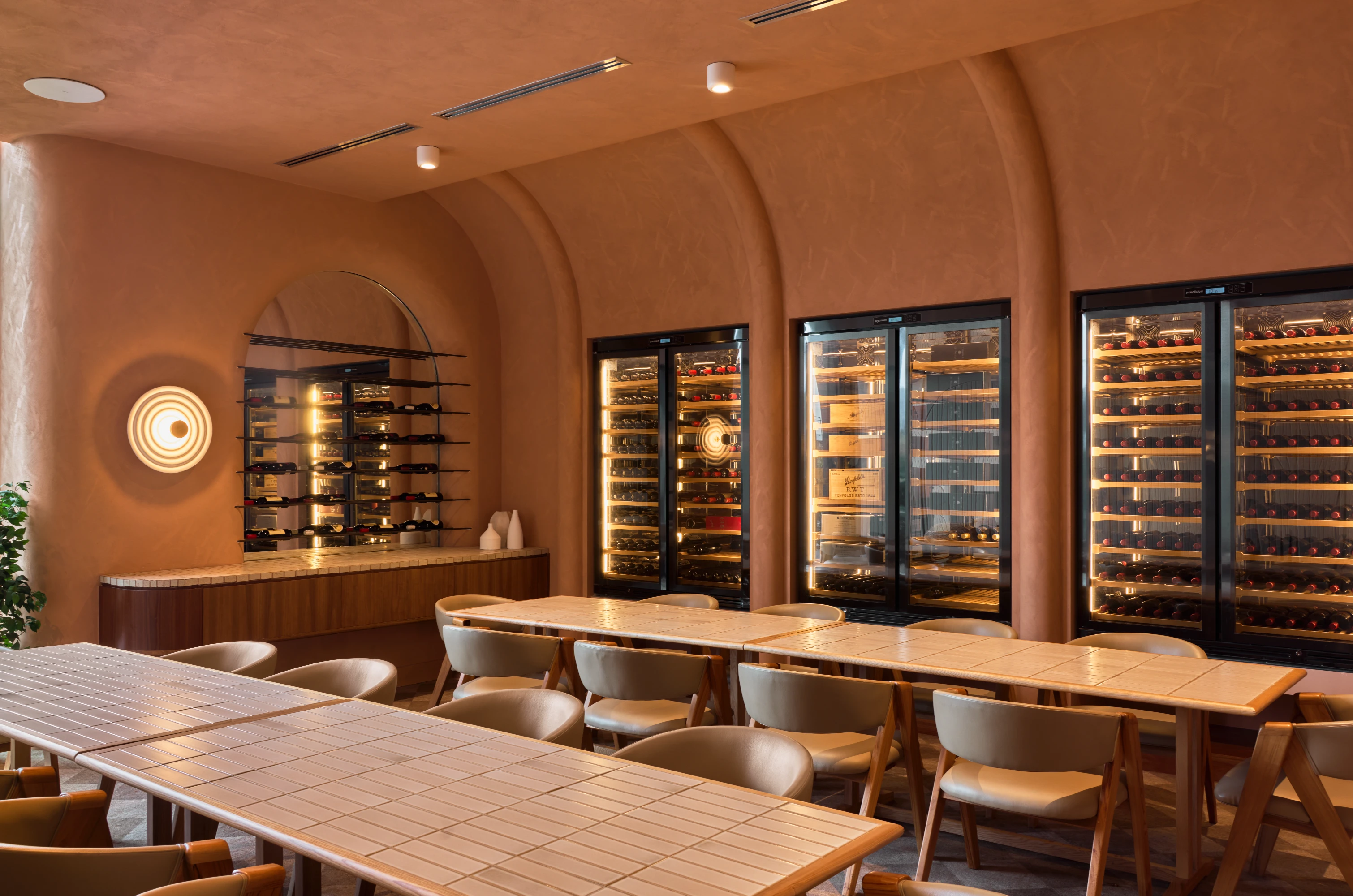 Modern wine cellar with rows of wine refrigerators and dining tables.