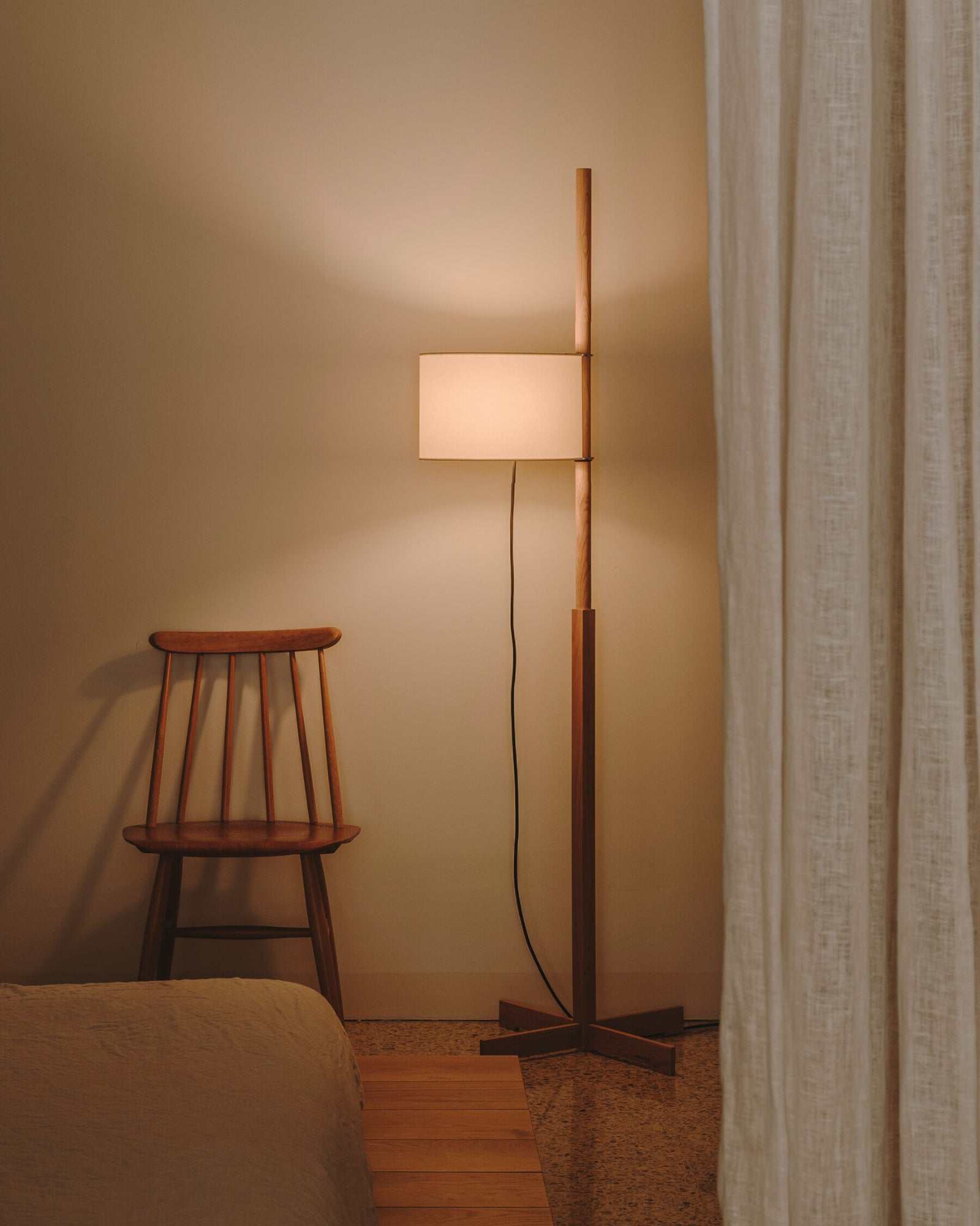 A TMM Floor Lamp within minimalist bedroom with soft linen curtains and wooden chair.