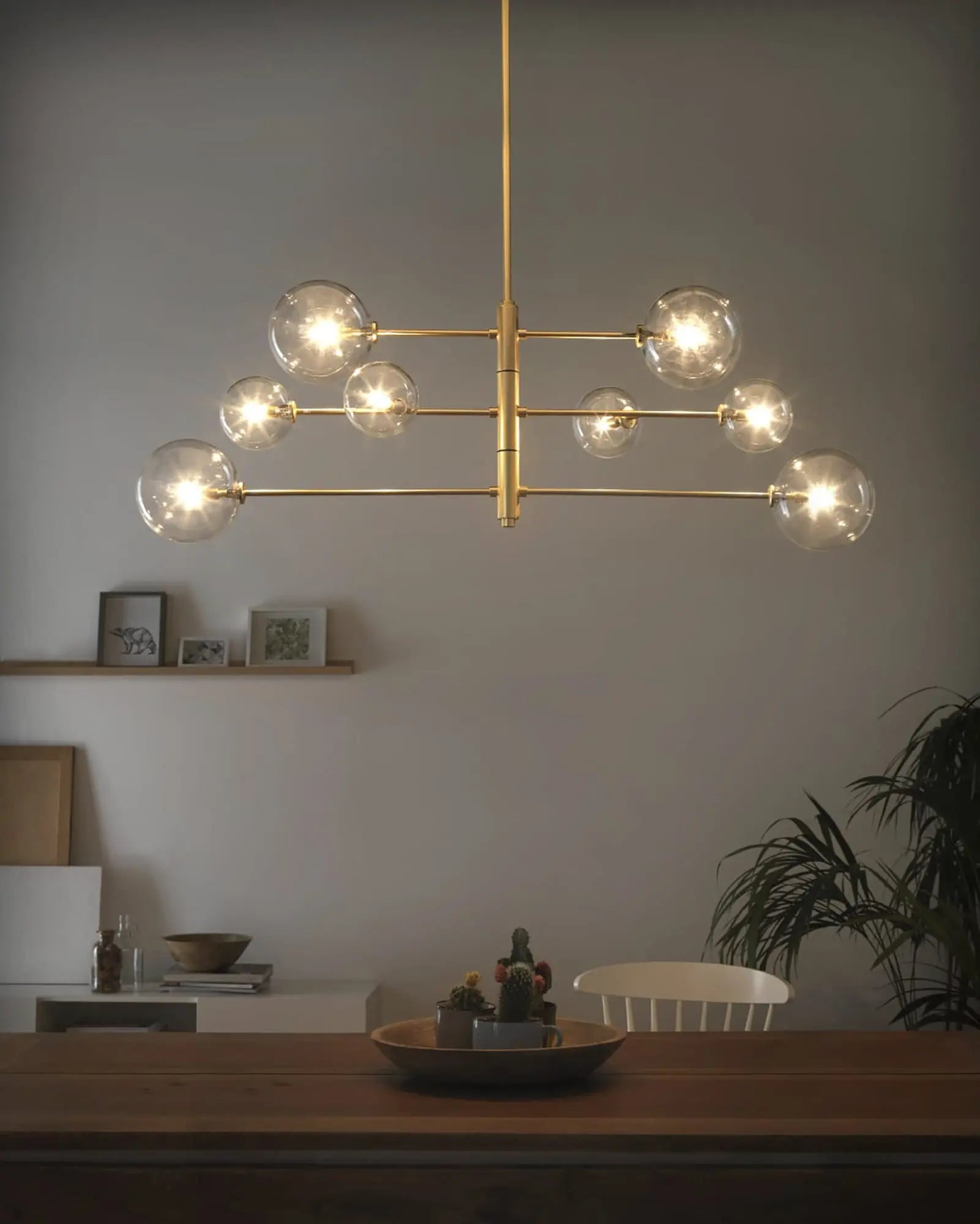 Atom contemporary adjustable pendant light in brass and clear glass orb shades above dining table