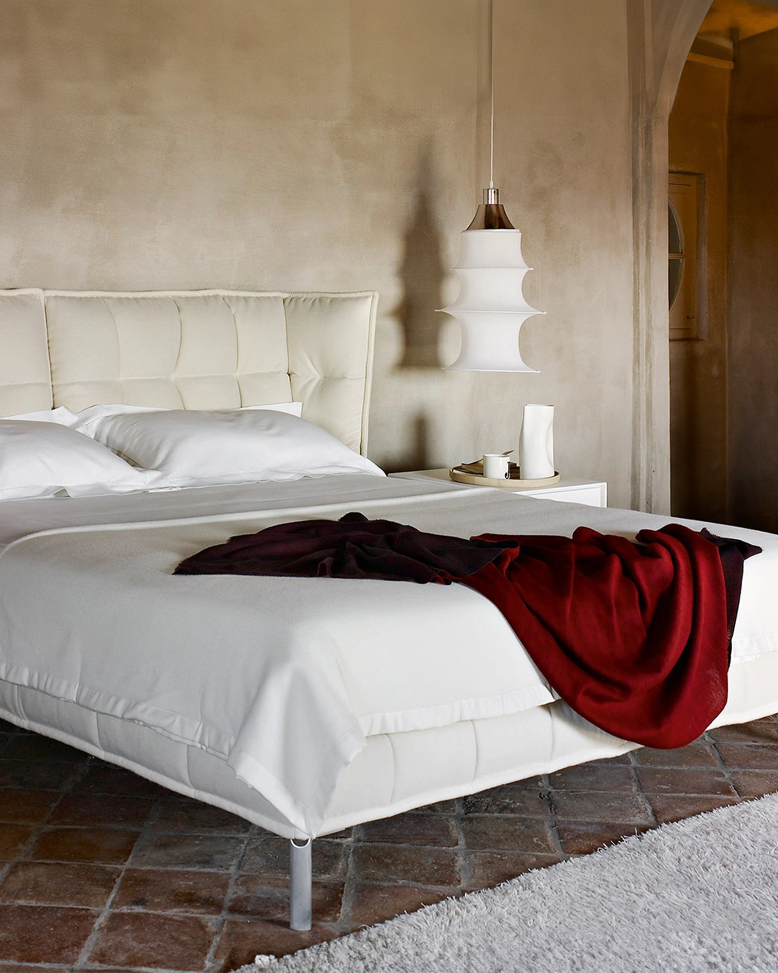 Modern bedroom with a white bed and red blanket on a tiled floor with Falkand Pendant Light by Artemide.