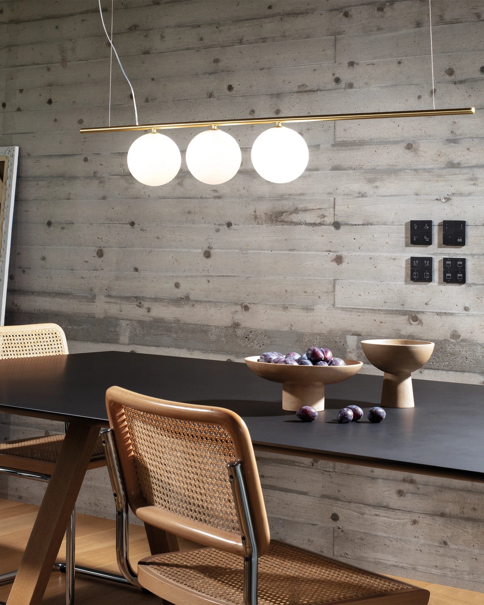 Modern dining area with a 3 light pendant light, table, and chairs against a wooden wall.