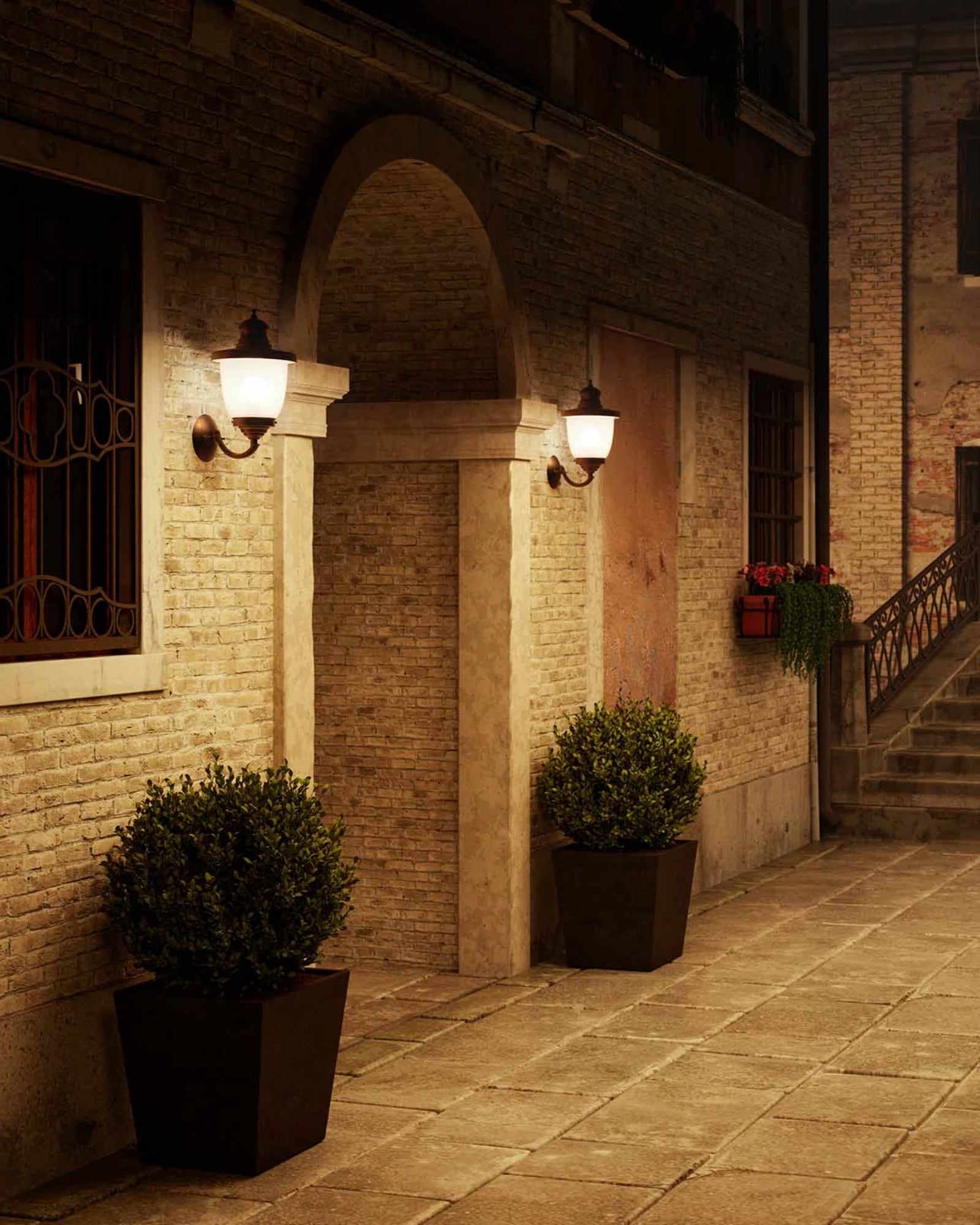 Street scene with potted plants and illuminated venezia up wall lights by Il Fanale on a building facade.