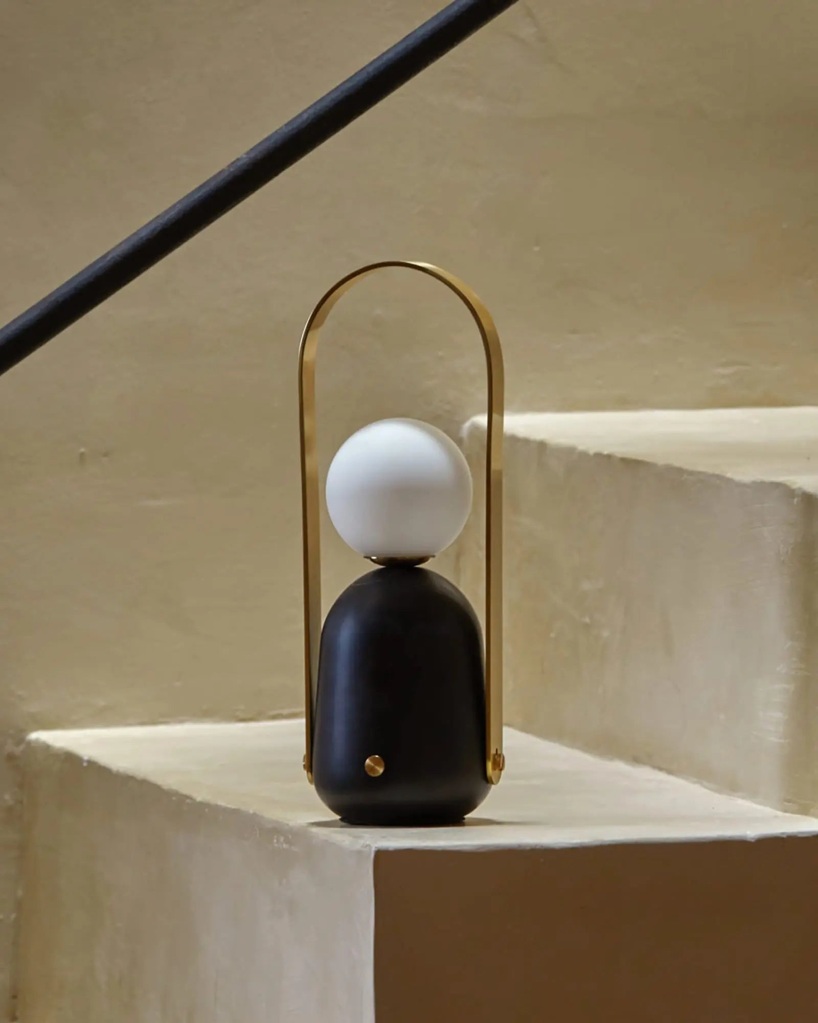 Nano Portable opal glass orb shade and brass handle table lamp on a staircase