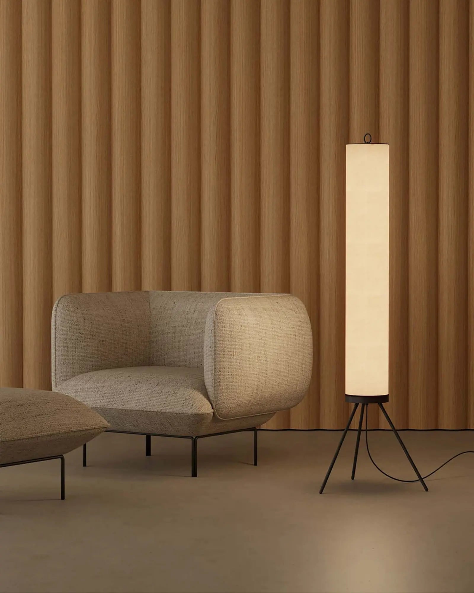 Nooi Floor lamp minimalistic cylinder with tripod base beside a sofa chair in lounge area